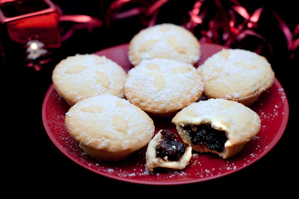 Sugar-dusted mince pies on a red plate, one broken open to show dark fruit filling