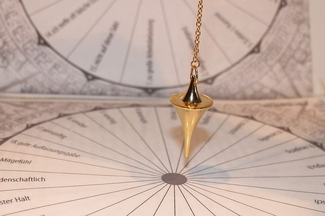 Brass conical pendulum hanging over a circular chart marked with radial German labels