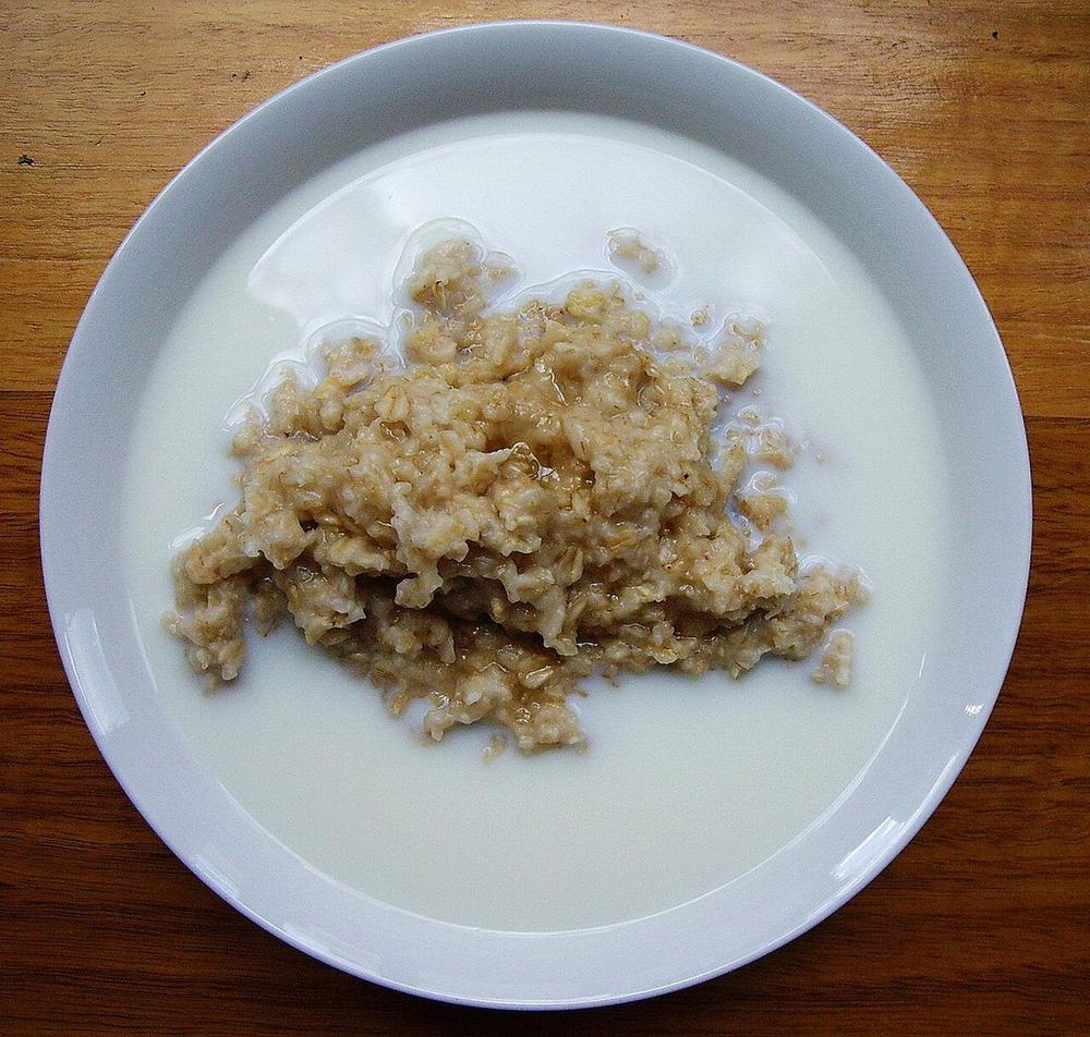White bowl of oatmeal porridge with milk around the edges and a glossy honey drizzle
