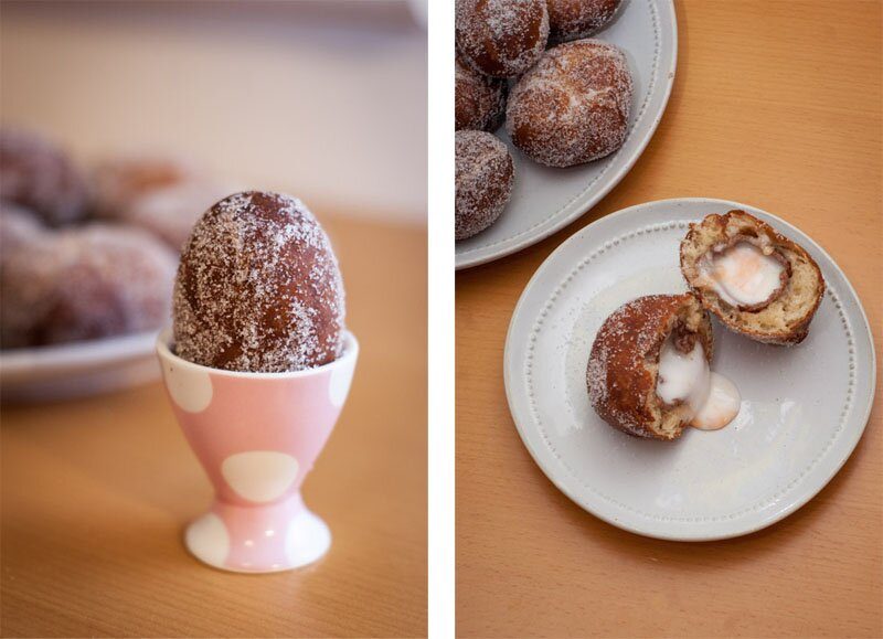 Sugar-coated egg-shaped doughnuts: one upright in a pink polka-dot egg cup, another halved to show white cream with an orange centre