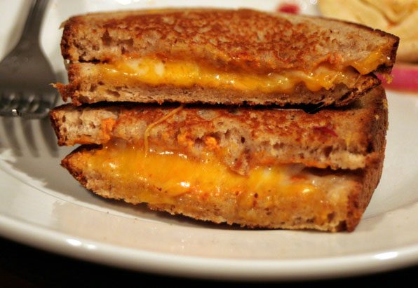 Grilled cheese toastie halves stacked on a white plate with melted cheese oozing from toasted bread