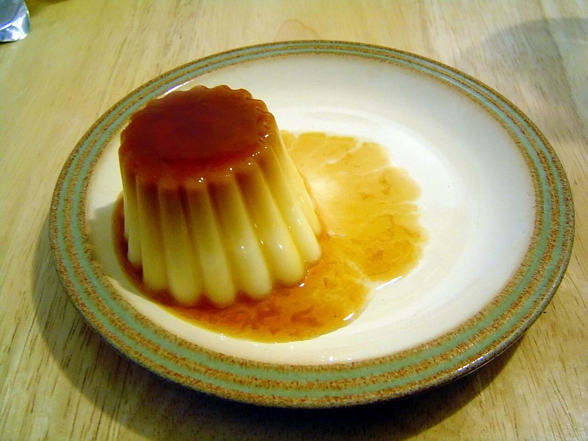 Fluted crème caramel on a patterned plate with dark amber caramel poured over the top