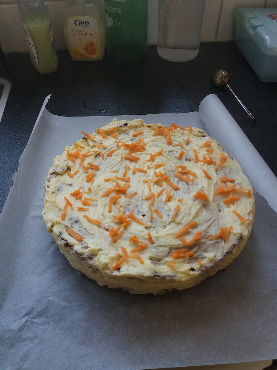 Round frosted cake topped with grated carrot on parchment paper on a kitchen counter