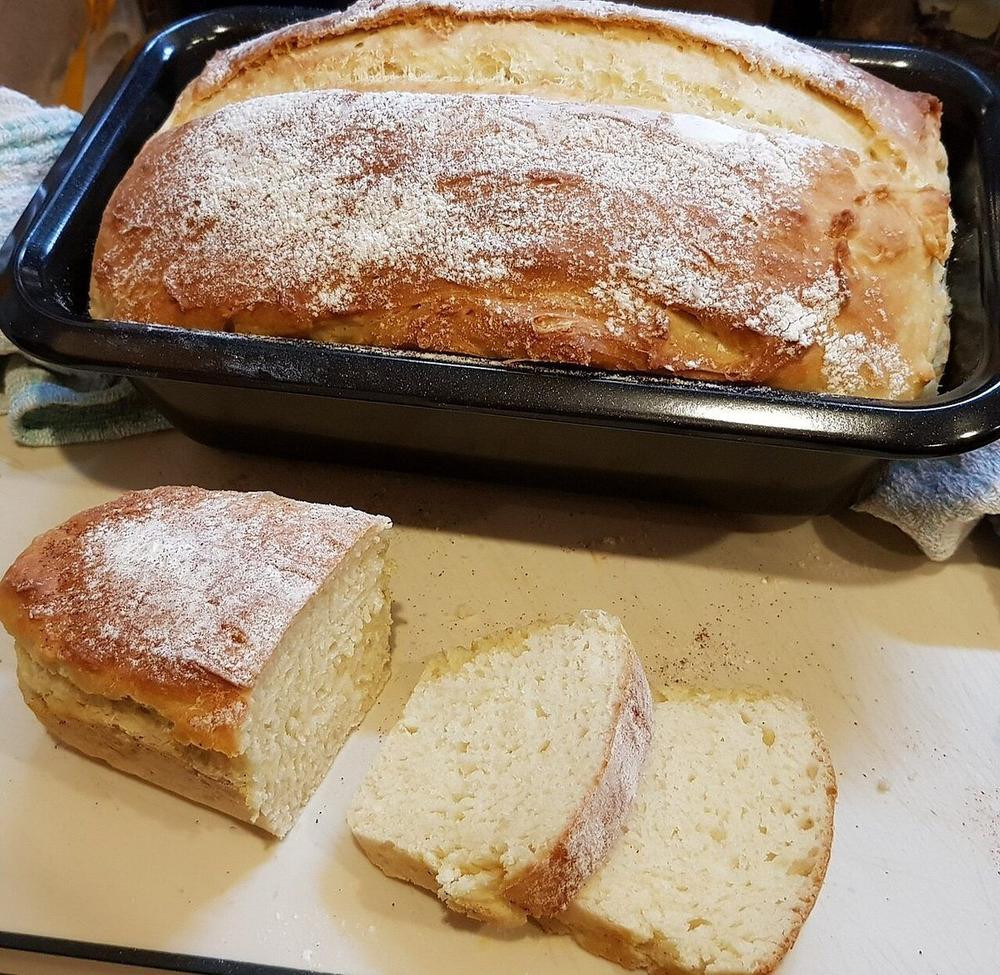 Flour-dusted golden loaf in a tin beside thick slices showing a soft white crumb