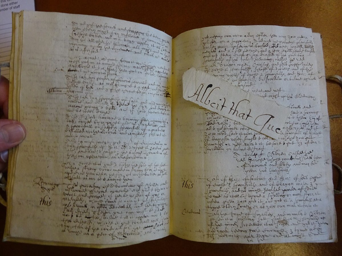 Open antique recipe manuscript with dense handwriting and a calligraphic scrap across the page