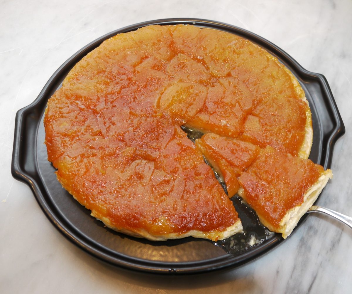 Caramelised tarte tatin on a dark platter with one slice lifted on a cake server