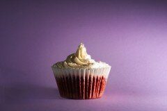 Red velvet cupcake in a white liner with a tall swirl of pale frosting and sugar crystals on purple