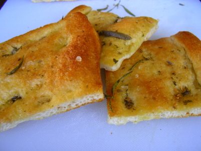 Three pieces of golden focaccia scattered with rosemary and coarse salt on a white surface