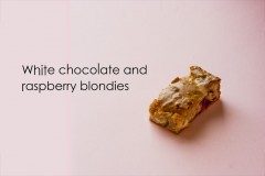 Rectangular blondie slice with white chocolate chunks and raspberry pieces on a pink backdrop