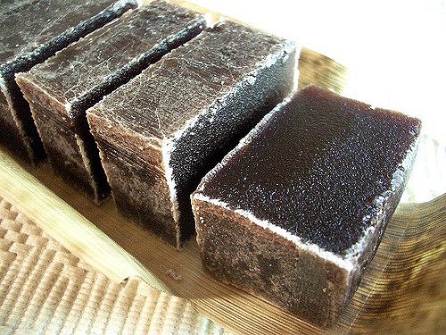 Dark rectangular blocks of dense Japanese yokan jelly arranged on a fibrous leaf tray