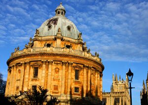 Radcliffe Camera’s circular stone dome and columns under a blue sky with a wrought-iron lamp